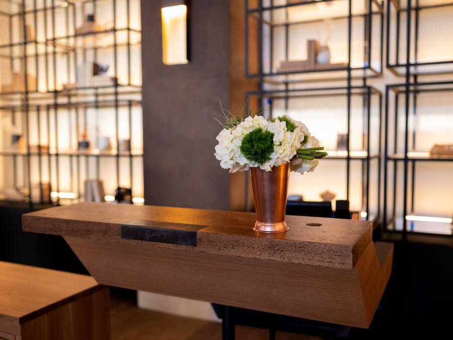 A reception desk with a vase of flowers, a nameplate, and a modern shelving unit in the background.