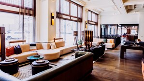 A spacious lounge area with a sofa set, a pool table, and large windows offering views of the street. - Surety Hotel, Autograph Collection (Des Moines)