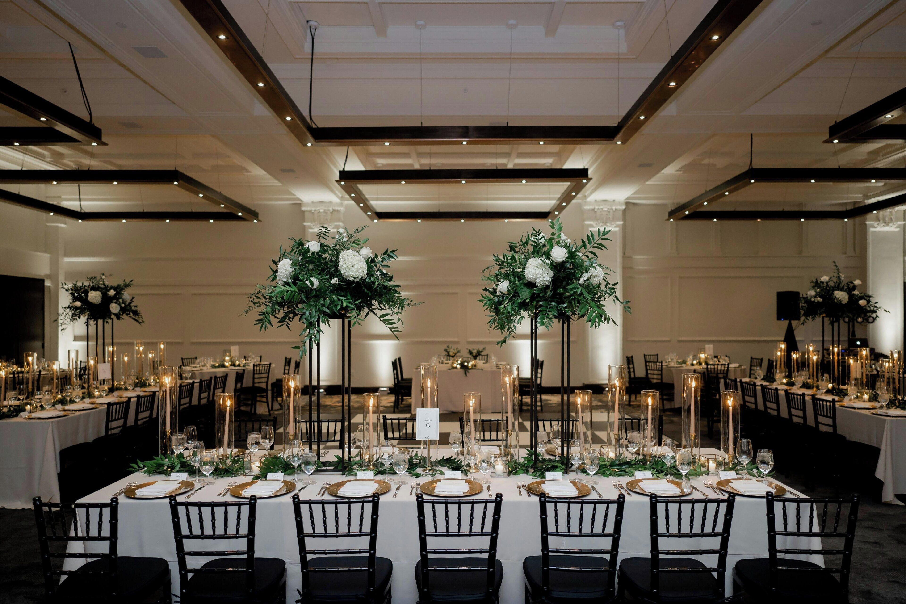Een balzaal met ronde tafels, zwarte stoelen en bloemrijke decoraties.