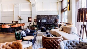 A spacious living area with a large black marble fireplace, leather sofas, and a modern bar area with orange chairs. - Surety Hotel, Autograph Collection (Des Moines)