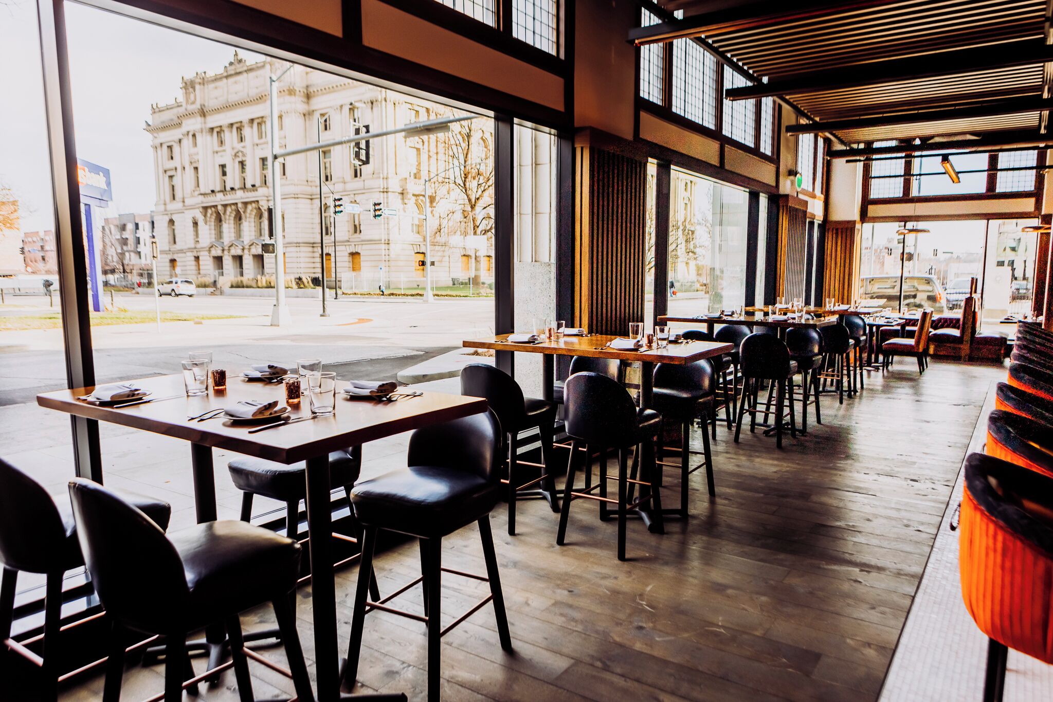 A restaurant with tables and chairs, large windows, and a view of a building outside.