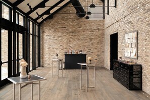 A spacious room with exposed brick walls, large windows, a bar area, and minimalist furniture.