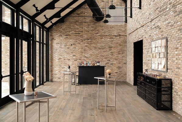 A spacious room with exposed brick walls, large windows, a bar area, and minimalist furniture.
