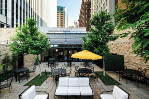 An outdoor patio with tables and chairs, a yellow umbrella, and a brick wall. - Surety Hotel, Autograph Collection (Des Moines)