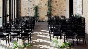 An indoor venue with a brick wall, black chairs arranged in rows, and hanging plants. - Surety Hotel, Autograph Collection (Des Moines)