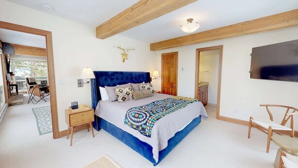 A bedroom with a large bed, wooden beams, a mounted TV, and a deer head decoration. - Shadowbrook (Snowmass Village)