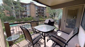 A balcony with a glass table and chairs, a pool in the background, and a view of multi-story buildings. - Shadowbrook (Snowmass Village)