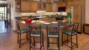A kitchen with wooden cabinets, a central island with bar stools, a refrigerator, and a microwave. - Shadowbrook (Snowmass Village)