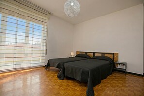 Une chambre avec deux lits, un plancher en bois, un luminaire au plafond et une fenêtre avec des stores.