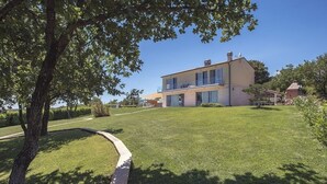 Une maison moderne à deux étages, dotée d’une grande pelouse et d’un arbre au premier plan.