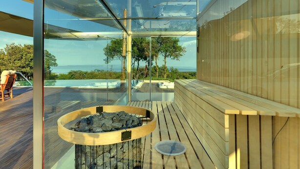 Un espace moderne aménagé à l’extérieur avec un bain à remous, une terrasse en bois, une enceinte en verre et une vue sur l’océan.