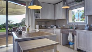 Une cuisine moderne dotée d’un grand îlot central, de luminaires suspendus et offrant une vue sur l’extérieur.