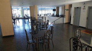 Un grand espace dédié à la salle à manger, avec plusieurs tables et chaises, un comptoir et de grandes fenêtres qui laissent entrer la lumière naturelle.