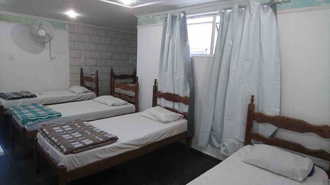 A room with three wooden beds, white bedding, and a window with white curtains.