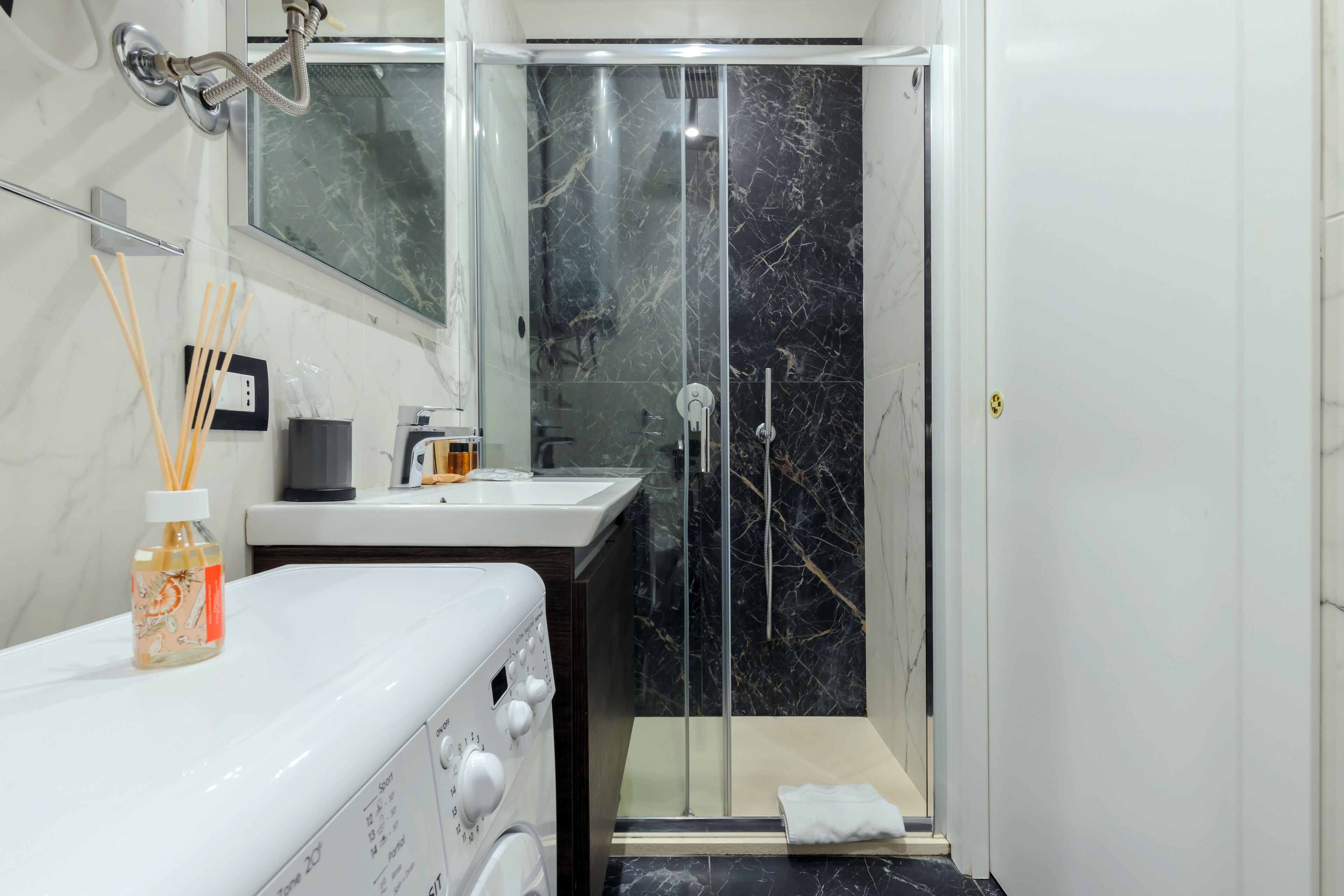 A modern bathroom with a glass-enclosed shower, a white sink, and a washing machine.