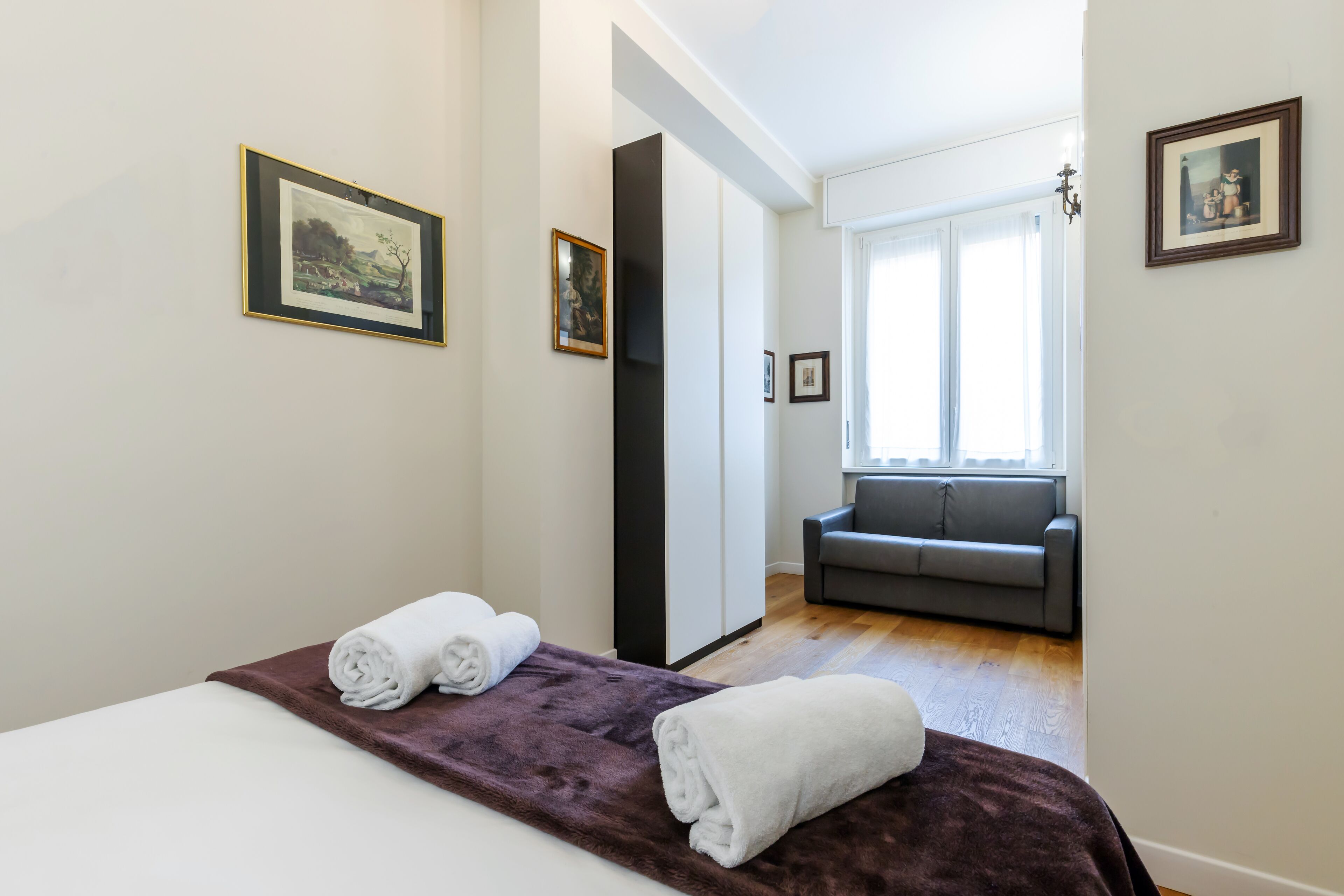 Ett hotellrum med en säng, en soffa och två inramade tavlor på väggarna.