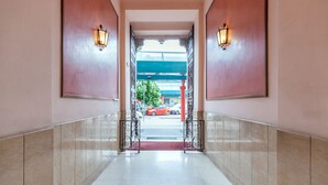 A hallway with a red carpet leading to an open door, flanked by two wall-mounted light fixtures. - Milan Retreats Cadorna (Milan)