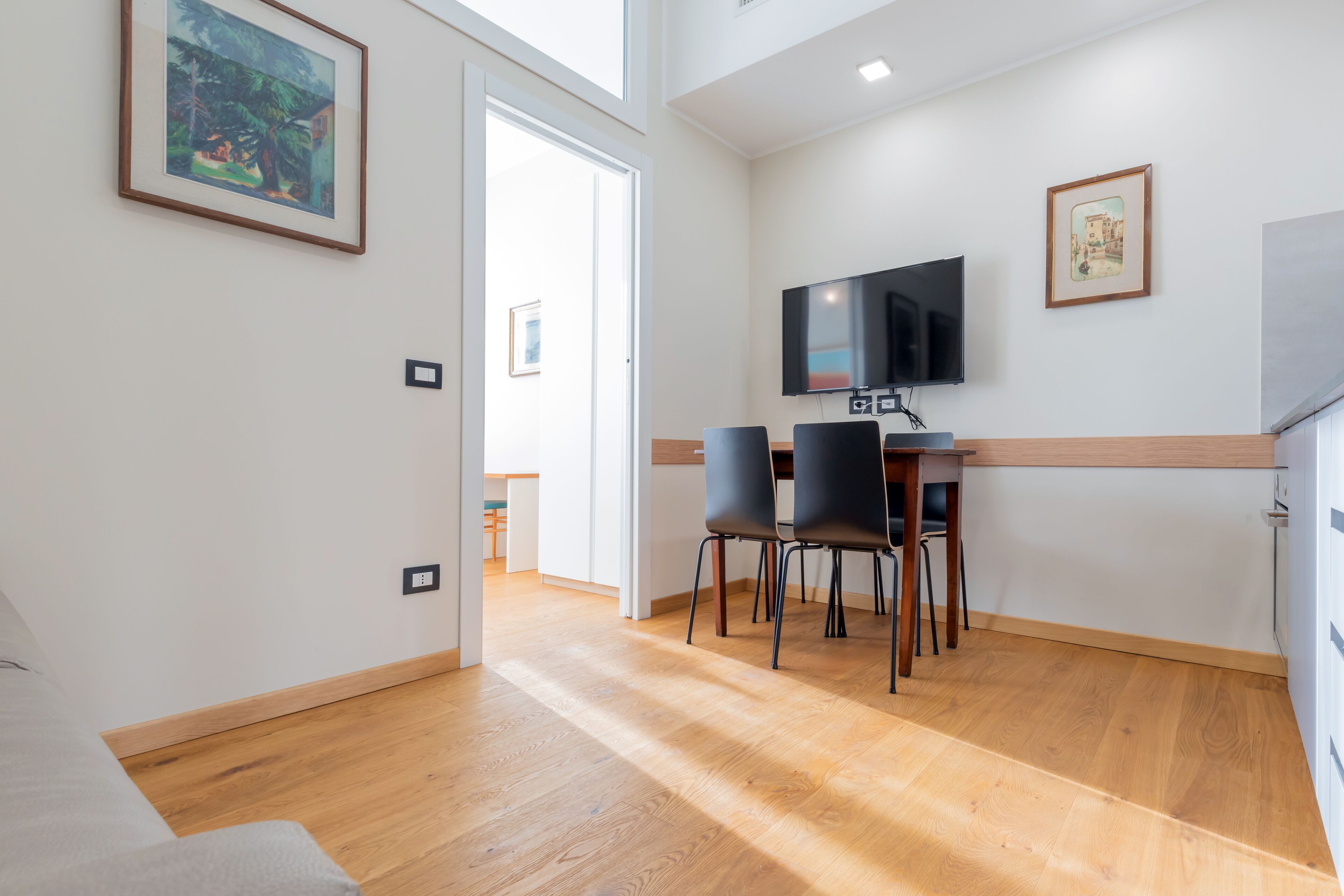 Une chambre moderne avec un plancher en bois, un coin repas avec des chaises, un téléviseur fixé au mur et un tableau accroché au mur.