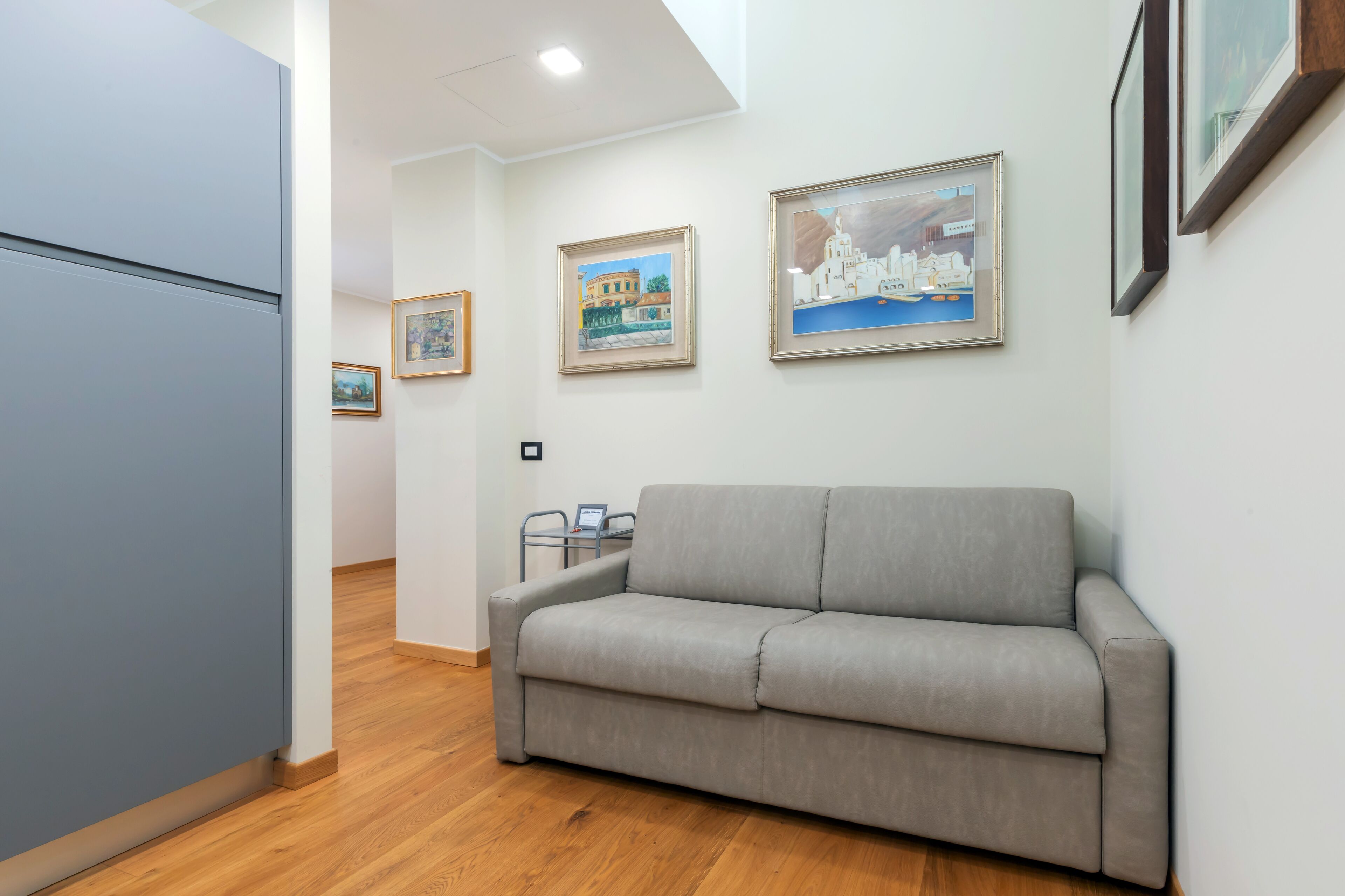 A modern living room with a grey sofa, wooden flooring, and framed artwork on the walls.