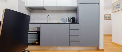 A modern kitchen with grey cabinets, a built-in oven, and a black chair in the foreground.