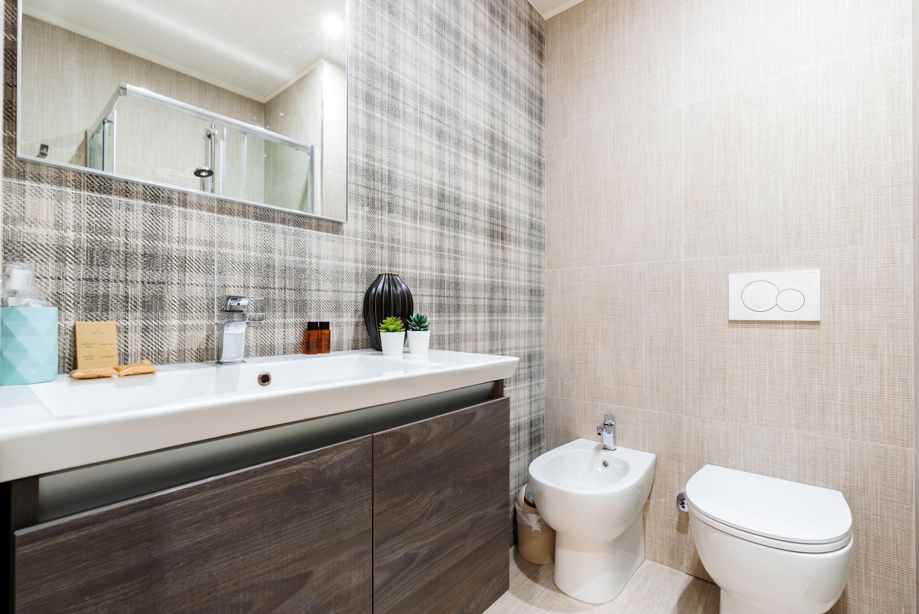 A modern bathroom with a large mirror, a white sink, a bidet, and a toilet.