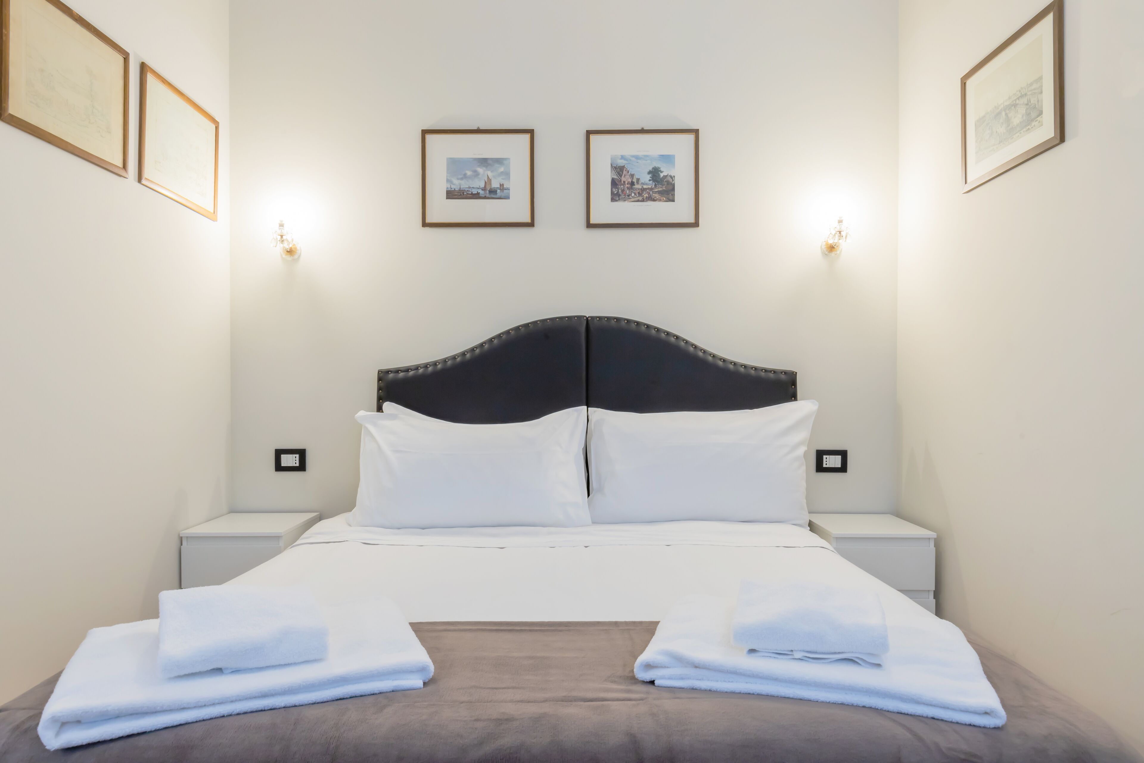 A neatly made bed with white linens and two pillows, flanked by two bedside tables with lamps.