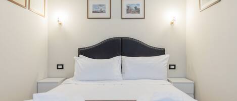 A neatly made bed with white linens and two pillows, flanked by two bedside tables with lamps.