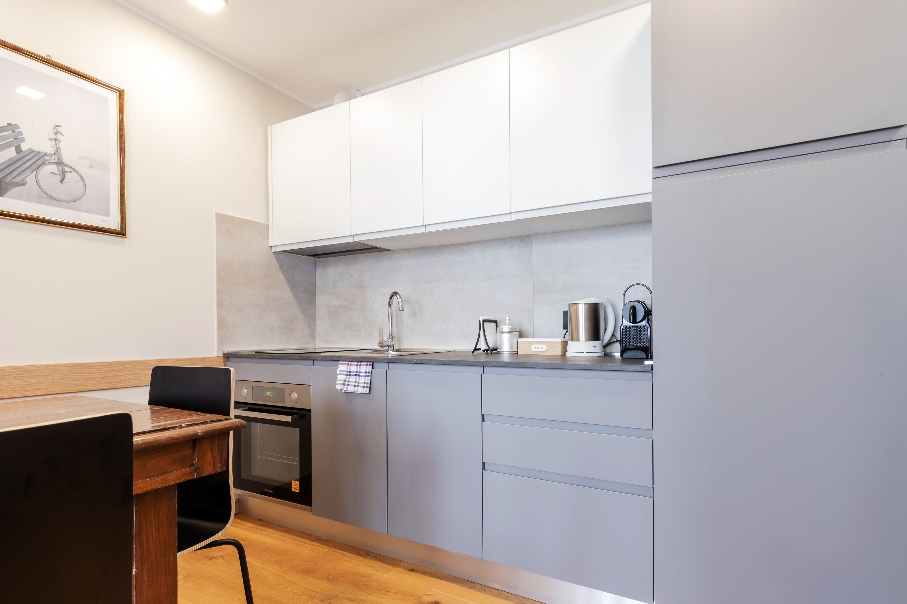 A modern kitchen with grey cabinets, a wooden dining table, and a framed picture on the wall.
