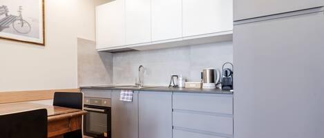 A modern kitchen with grey cabinets, a wooden dining table, and a framed picture on the wall.