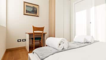 A hotel room with a bed, a desk, a chair, and a painting on the wall.