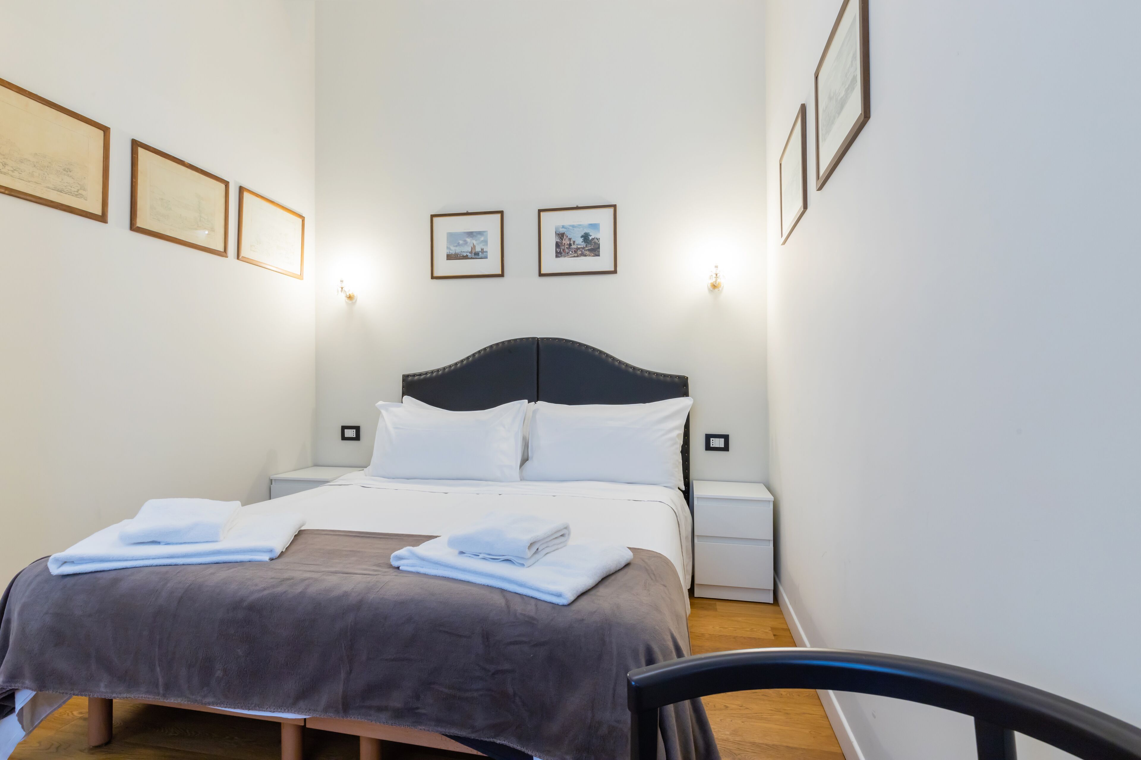 A neatly made bed with white linens and a dark headboard, flanked by two bedside tables with lamps.