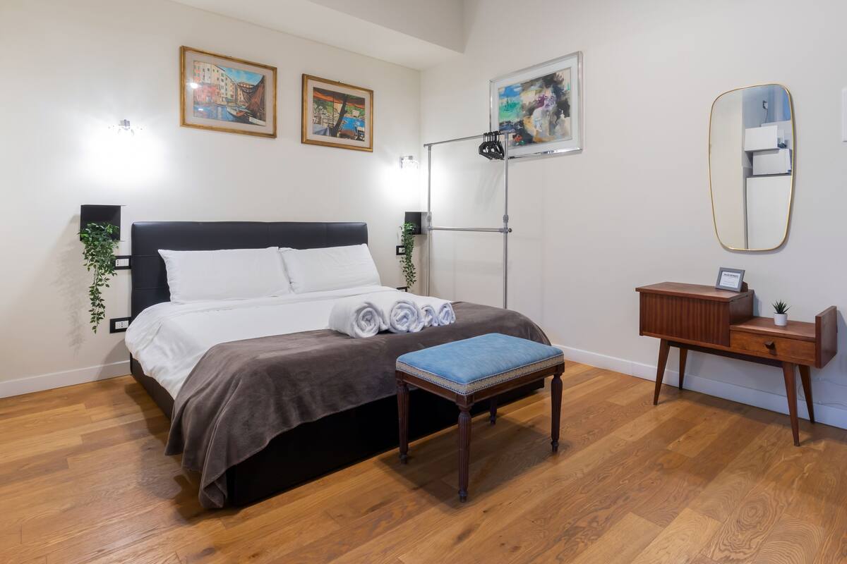 A neatly arranged bedroom with a bed, bedside table, bench, and a mirror.