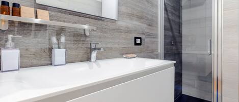 Un baño moderno con tocador blanco, cabina de ducha con mampara de vidrio y salpicadero de mármol.