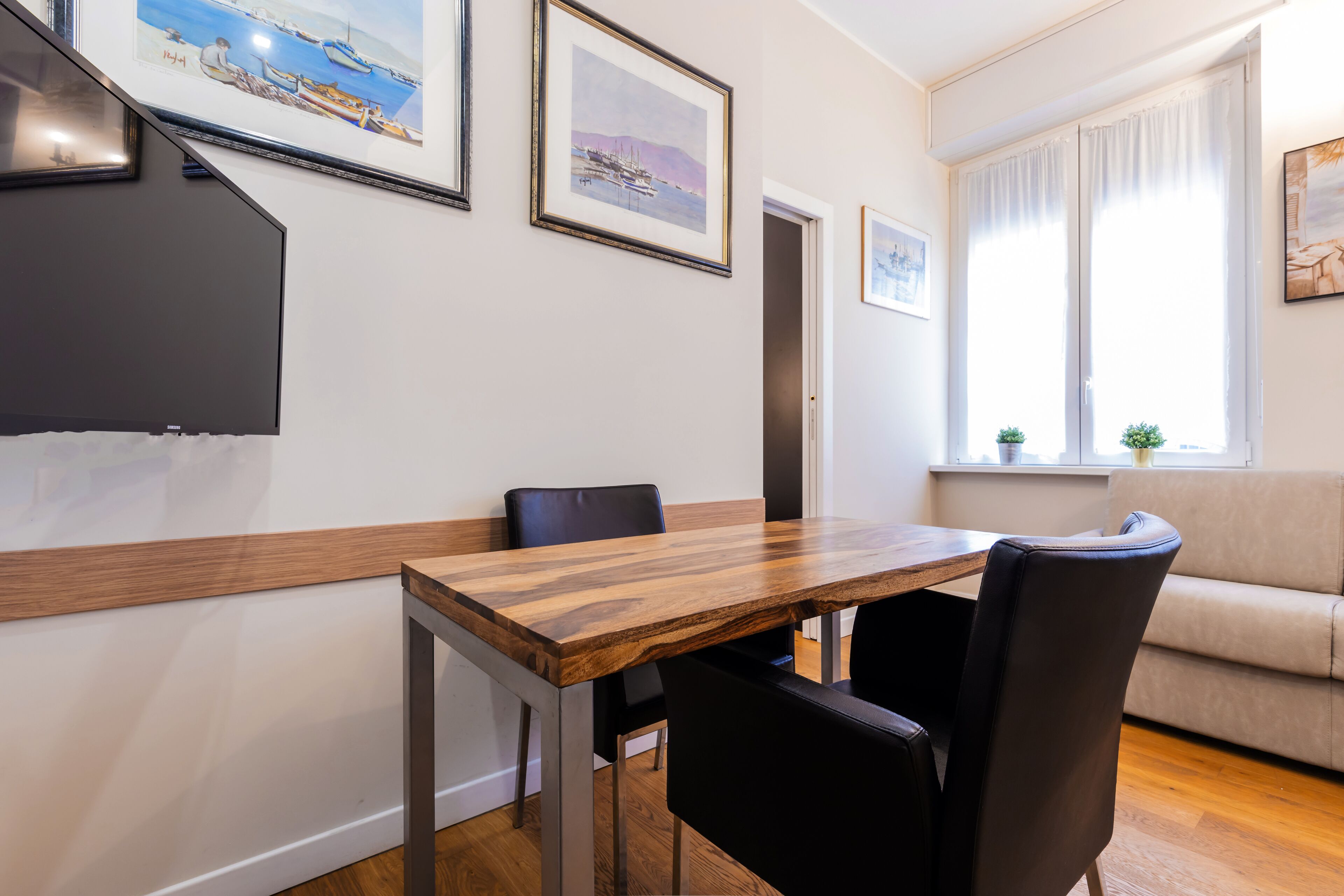 A dining area with a wooden table and black chairs, a sofa, and framed artwork on the walls.