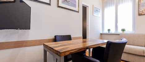 A dining area with a wooden table and black chairs, a sofa, and framed artwork on the walls.