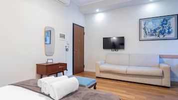 Ein Hotelzimmer mit einem Bett, einem Holznachttisch, einem kleinen Tisch, einem beigen Sofa, einem Flachbildfernseher und einem gerahmten Kunstwerk an der Wand.