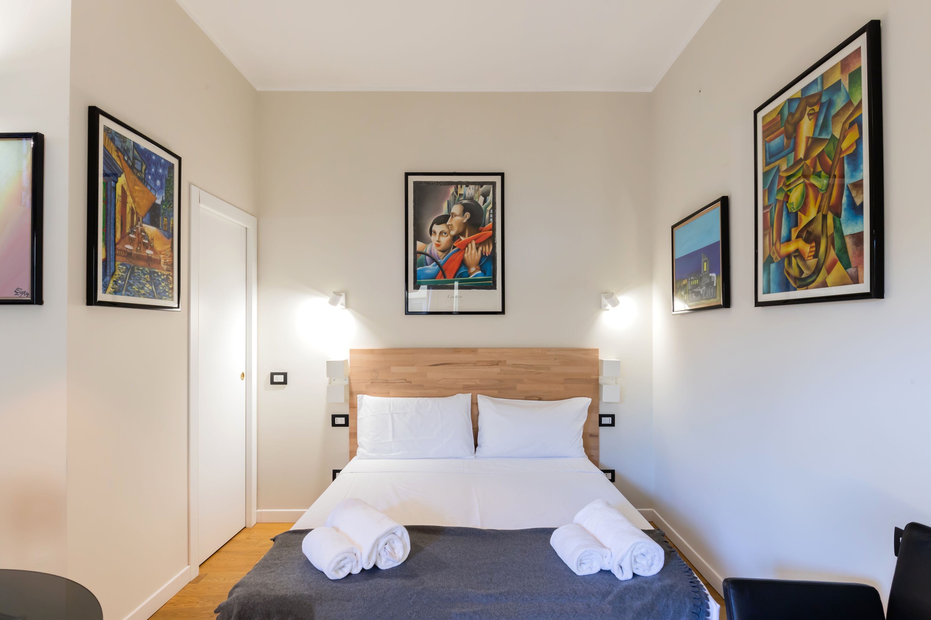 Una habitación de hotel con cabecera de madera, ropa de cama blanca y obras de arte en las paredes.