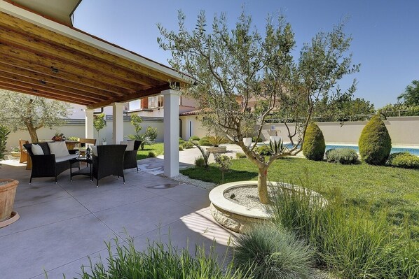 A covered patio area with outdoor furniture, a small tree, and a well-maintained lawn.