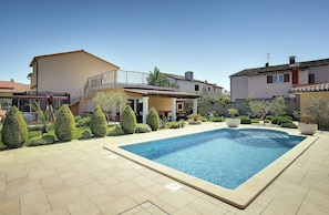 A residential property with a swimming pool, a covered patio, and a garden with neatly trimmed bushes.