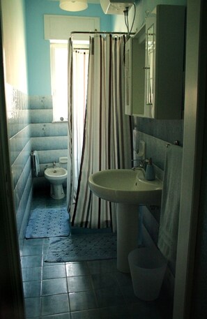 A bathroom with a shower curtain, a sink, a toilet, and a mirror. - B&B La Lampara (Castellabate)