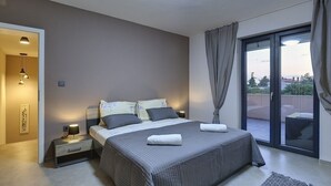 A modern bedroom with a large bed, a nightstand, a lamp, and a view of the outdoors through a sliding glass door. - Comfortable villa with private pool, just 1.5 km to the beach (Fazana)