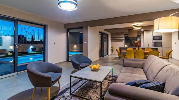 A modern living room with a sofa, armchairs, a coffee table, and a dining area with yellow chairs. - Comfortable villa with private pool, just 1.5 km to the beach (Fazana)