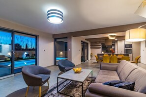 Uma sala de estar moderna com um sofá, poltronas, uma mesa de centro e um espaço de jantar com cadeiras amarelas.
