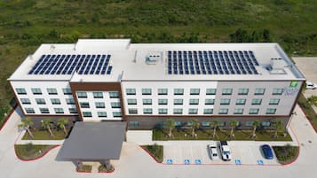 Un edificio moderno con paneles solares en el techo, un estacionamiento con espacios para discapacitados y un letrero de Holiday Inn Express.