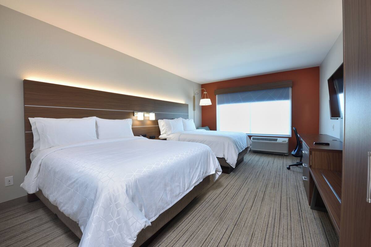 Una habitación de hotel con dos camas, un escritorio, una silla, un televisor y un ventanal amplio.