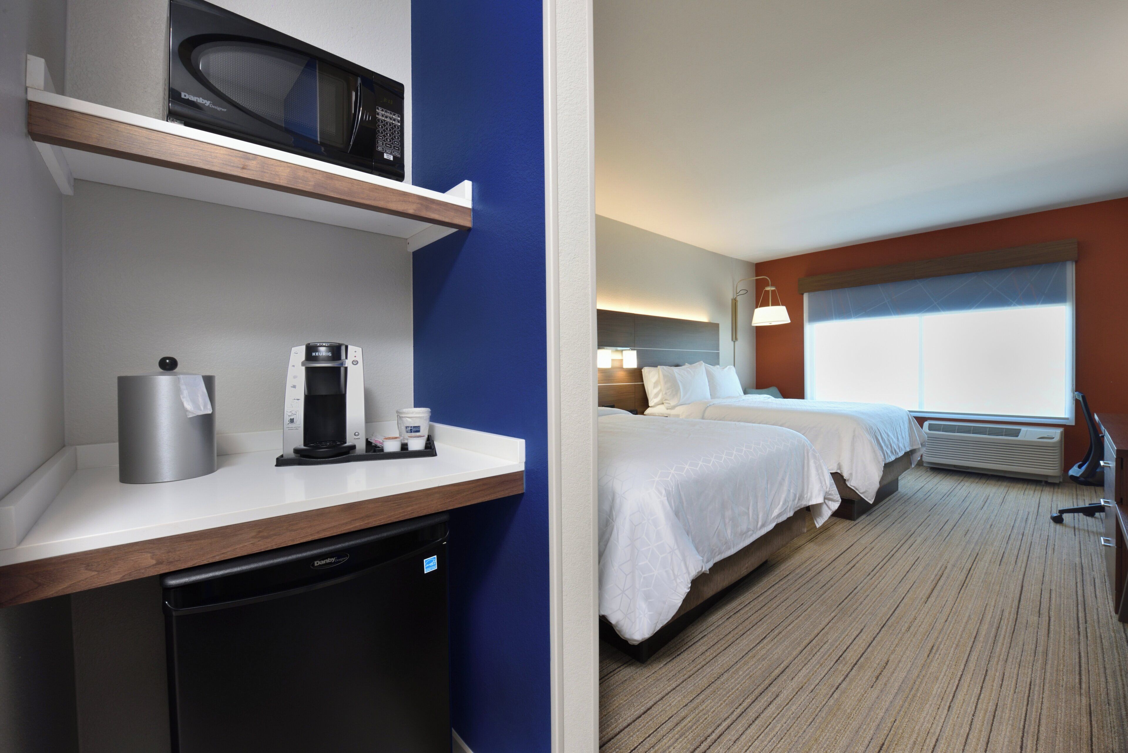 A hotel room with a kitchenette, a bed, a window, and a bedside table.