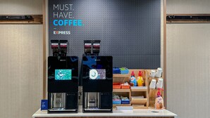 A coffee station with two coffee machines, a sign above stating "MUST HAVE COFFEE", and various coffee-related products on shelves.