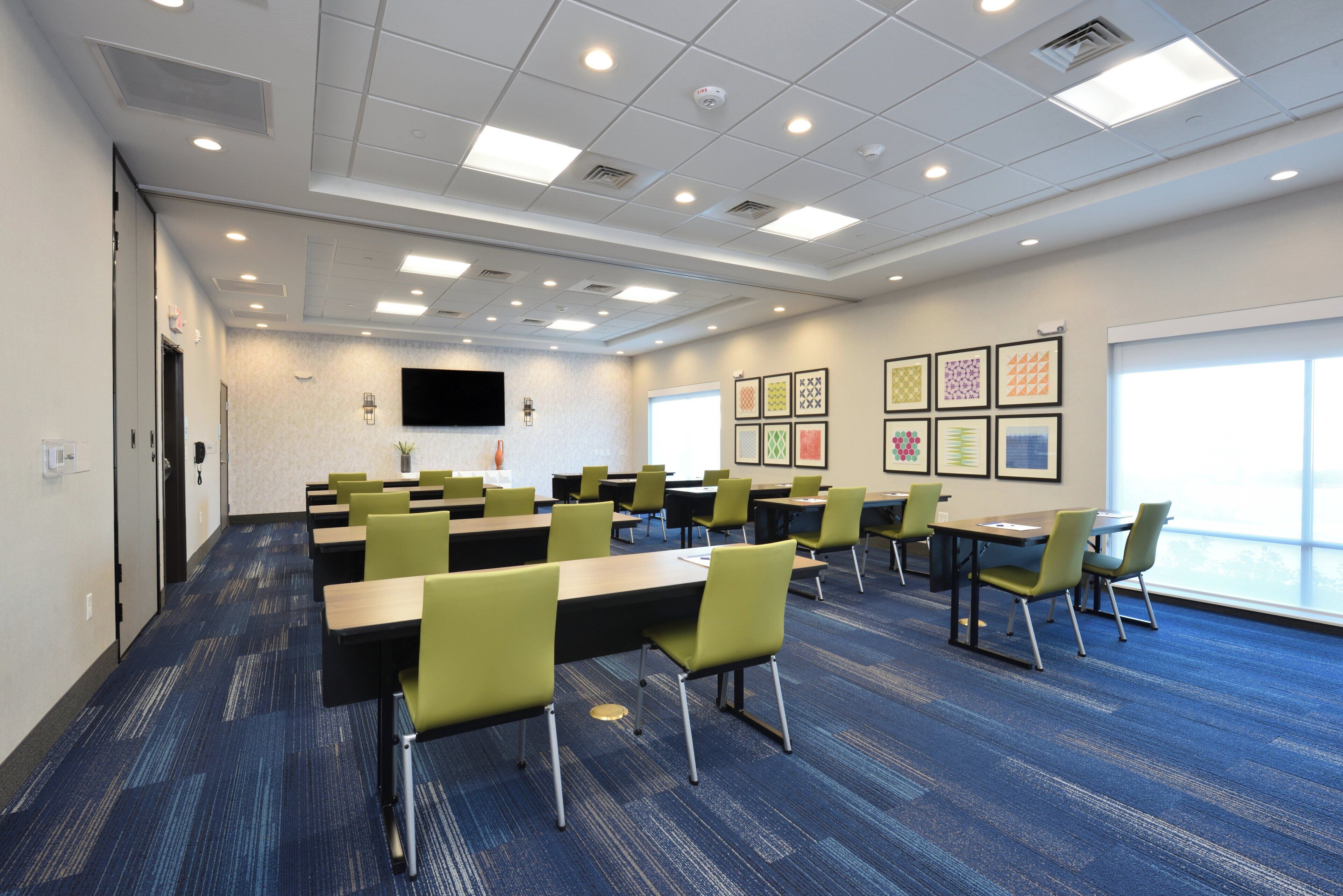 A conference room with multiple tables and chairs, a flat-screen TV mounted on the wall, and framed artwork on the wall.