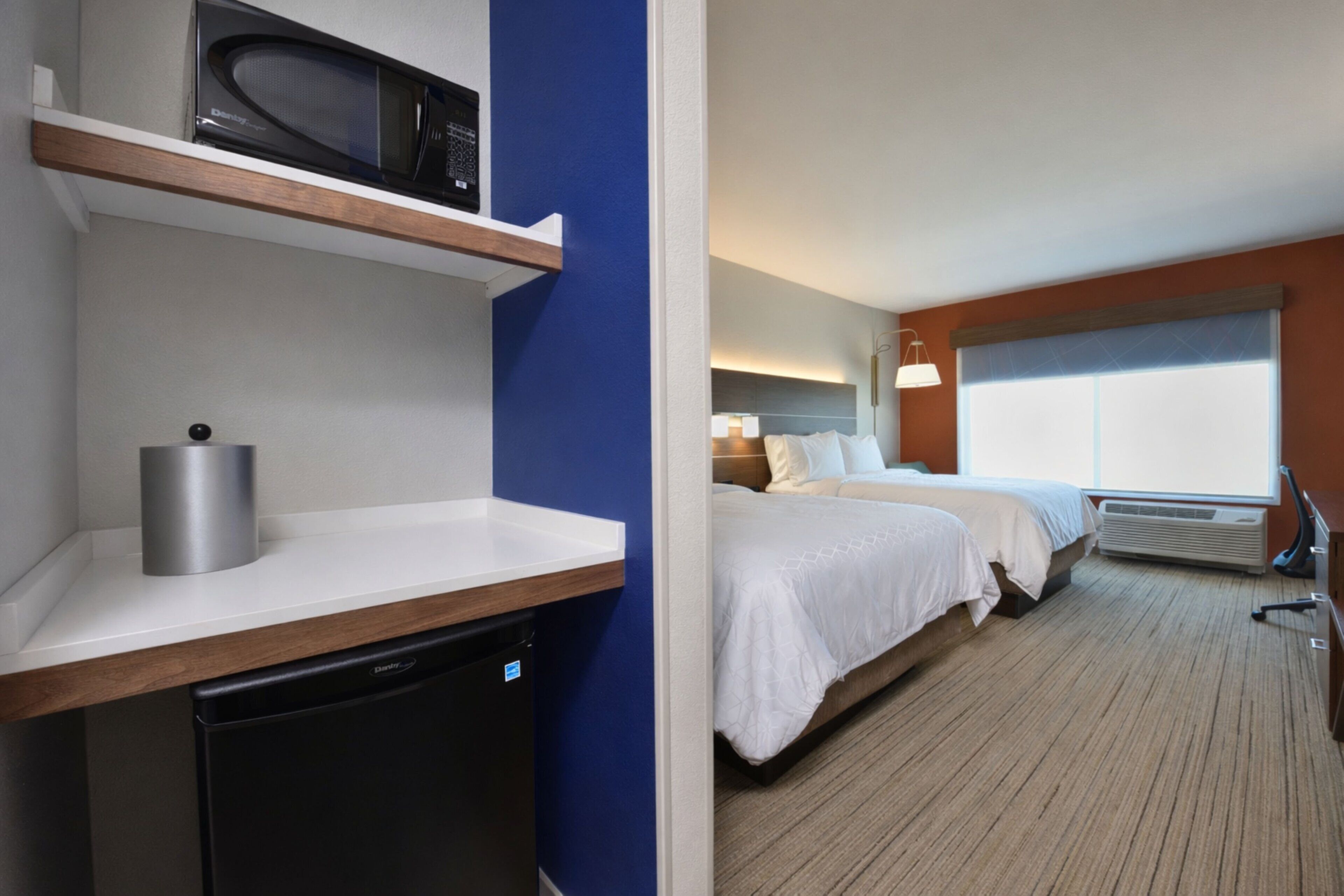 Une chambre d’hôtel avec un lit, une table de chevet et un four à micro-ondes posé sur une étagère.