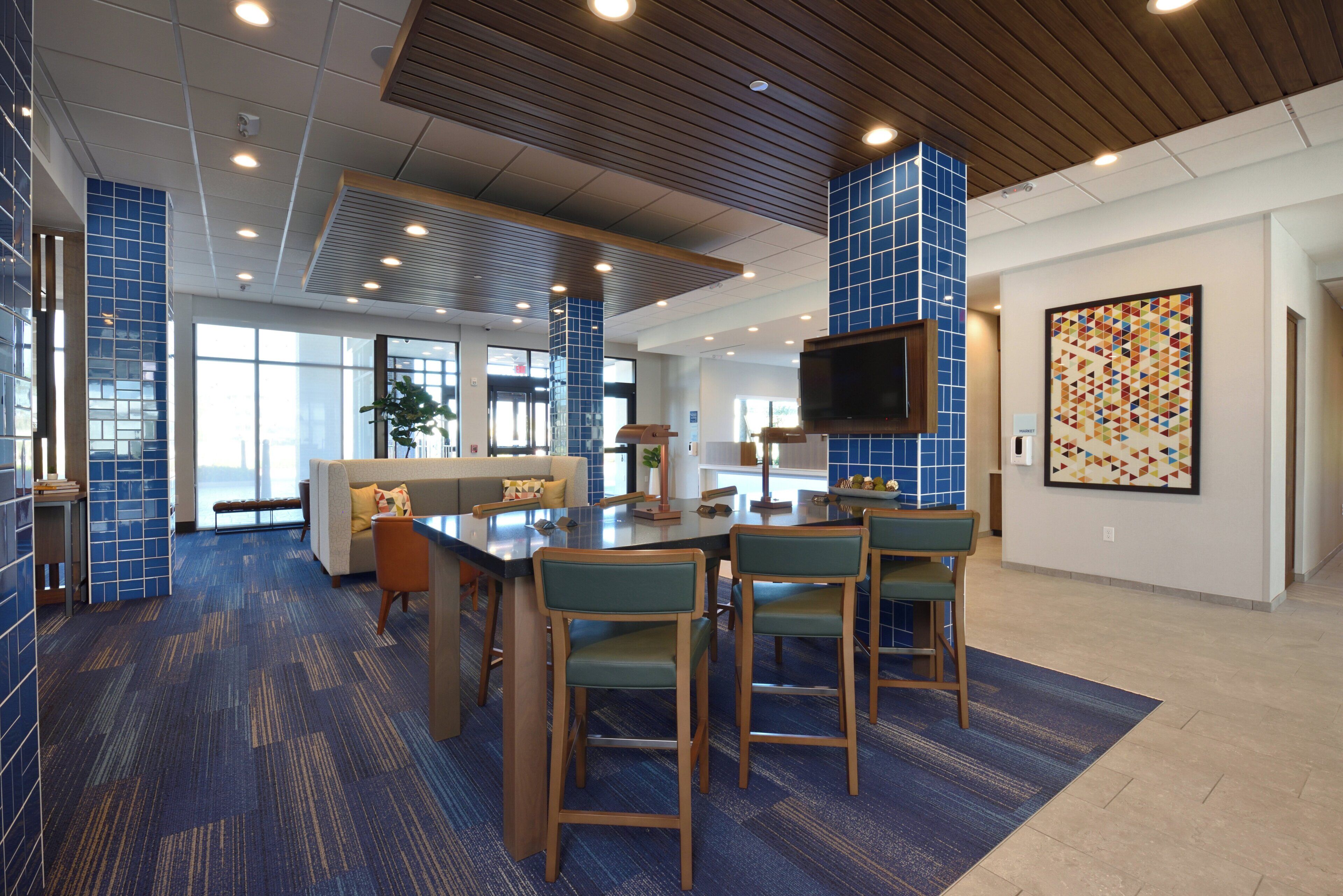 A modern hotel lobby with a bar area, seating, and a large TV screen.